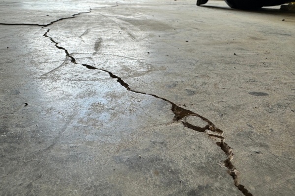 Close-up of cracked garage floor in Florida home caused by soil shifting and moisture, showing the need for professional concrete repair.