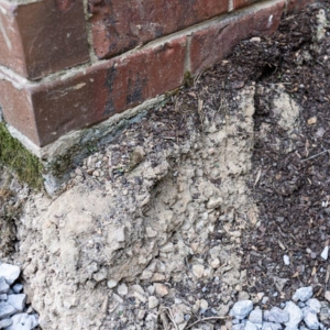 Sandy soil erosion near the foundation edge that causes uneven concrete slab settlement in Palm Coast, FL.