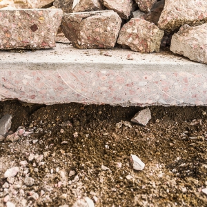 Eroded soil beneath a concrete walkway, showing voids and settlement causing sidewalk cracks in Palm Coast, FL.