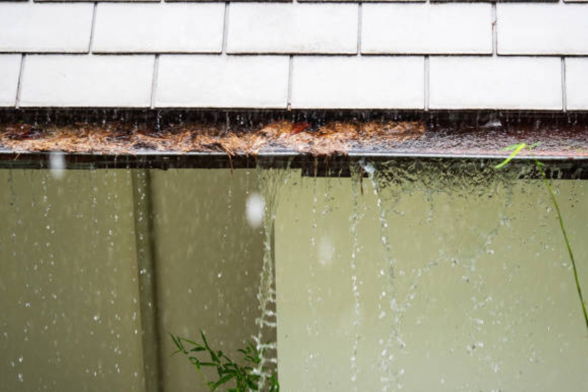 Overflowing gutters spilling water beside a home, causing foundation erosion in Palm Coast, FL.