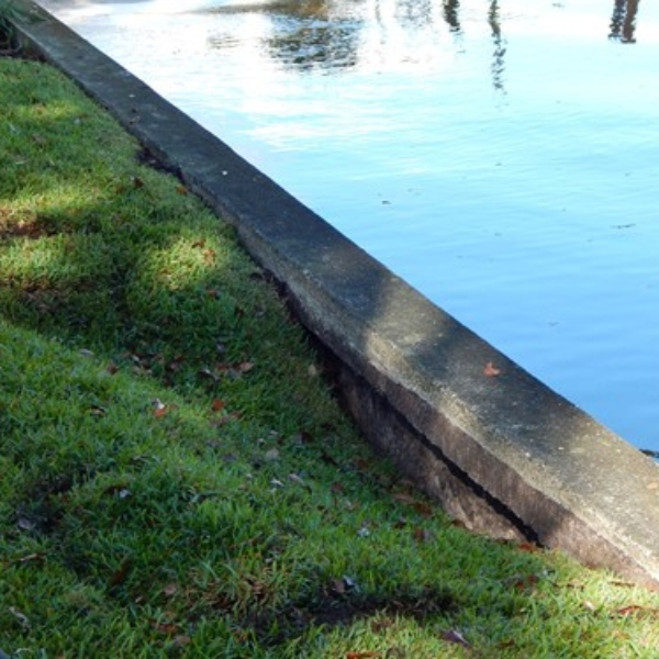 Close-up of concrete seawall with visible cracks and soil loss behind it, showing erosion damage needing seawall erosion repair in Northern Florida.