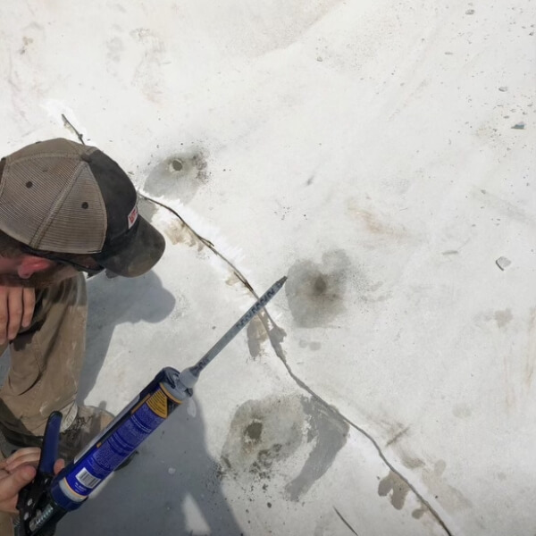 A technician caulking cracks in a concrete slab to stop water intrusion beneath the surface, a soil washout repair in Orange Park, FL.