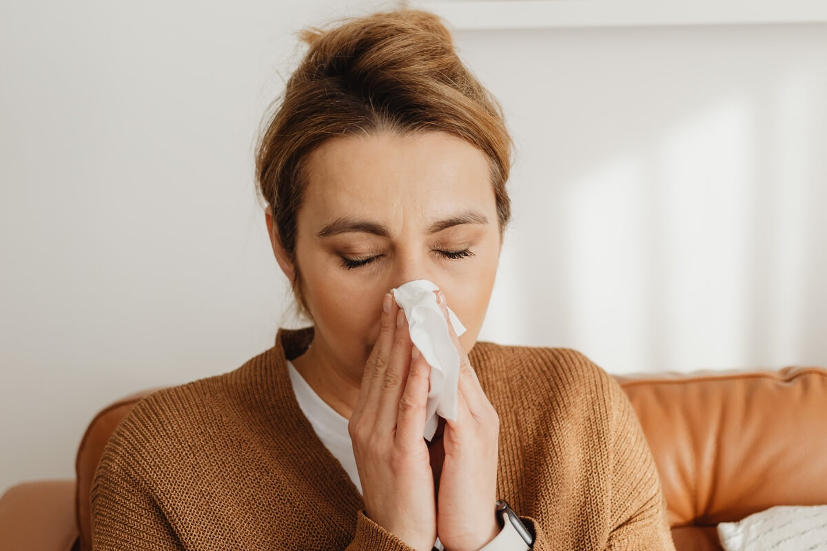 A woman sneezing indoors, showing how poor air quality from crawl space stack effect can trigger irritation in St. Augustine, FL.