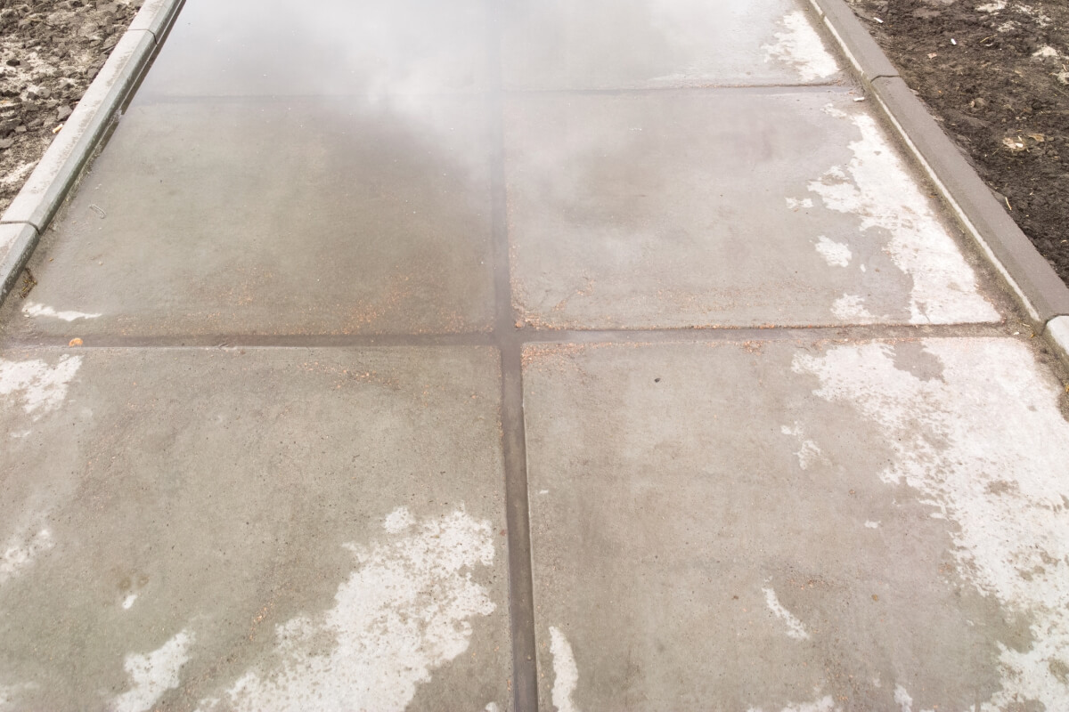 Rainwater pooling on an uneven concrete walkway, a sign of tree roots lifting concrete in Gainesville, FL.