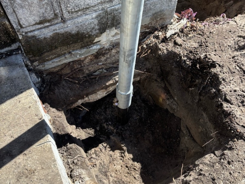 Helical pier installation beneath porch footing to stabilize settling concrete front porch foundation in St. Augustine, FL.