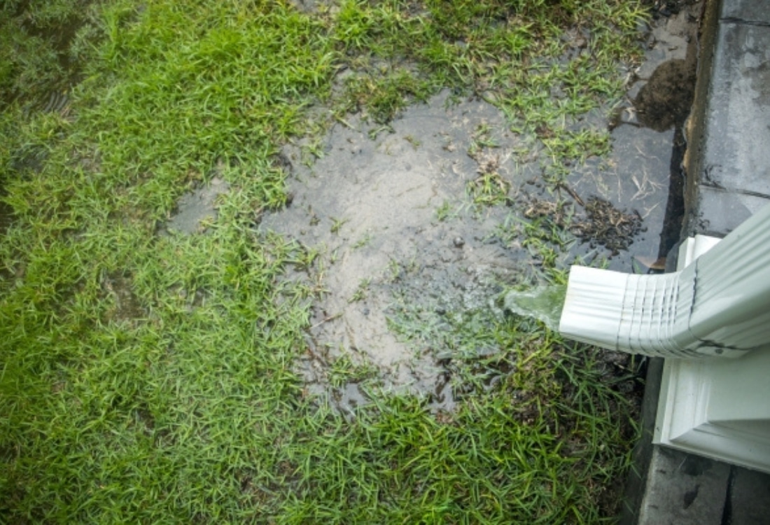 Downspout discharging rainwater directly at the base of a Jacksonville, FL, home, causing water pooling next to the foundation.