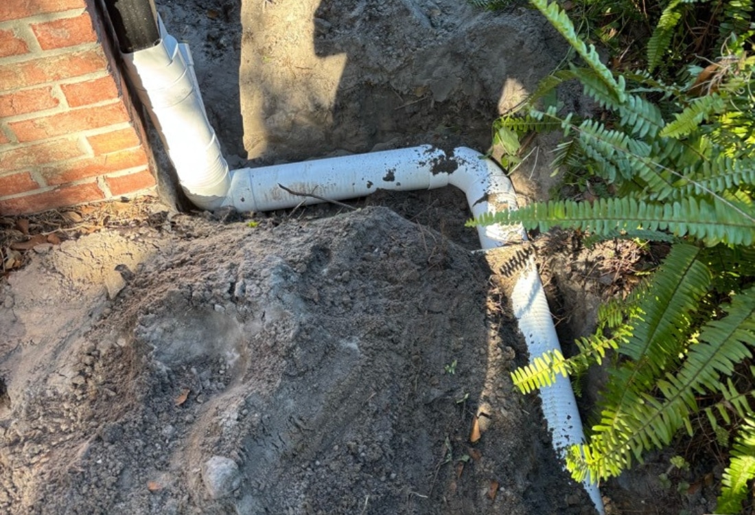 Downspout connected to white PVC pipe routed underground replacing corrugated extension after drainage installation in Jacksonville, FL.
