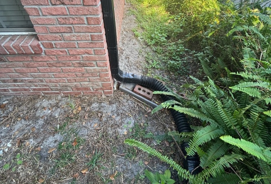 Corrugated flex downspout discharging water at foundation base before drainage downspout extension installation in Jacksonville, FL.