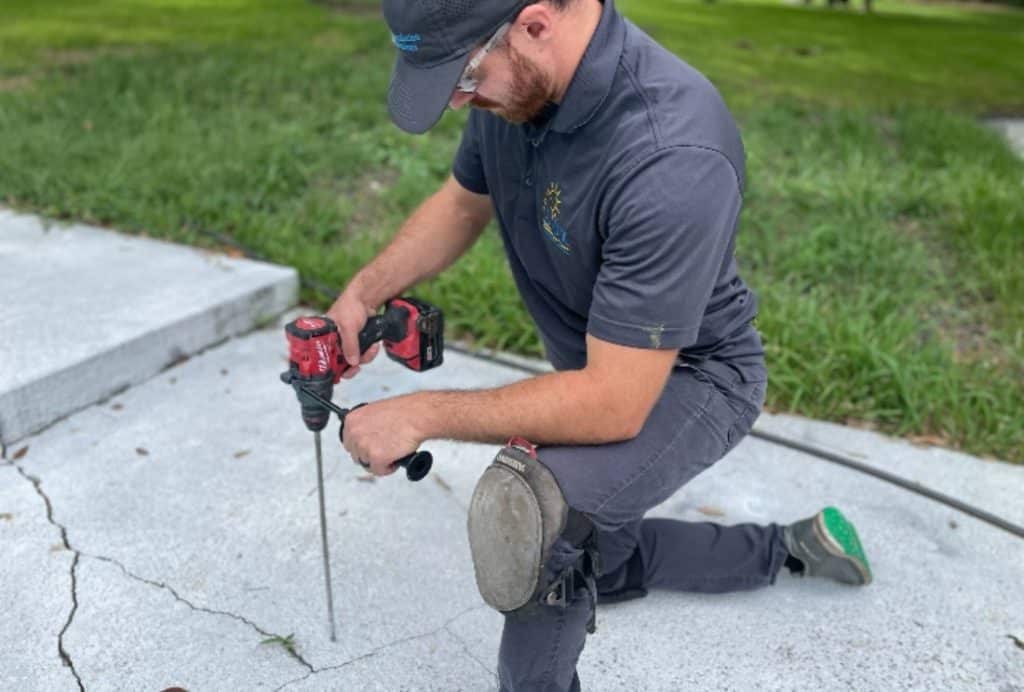 Technician drilling holes in a cracked driveway to inject polyurethane foam for concrete driveway crack repair in St Augustine, FL.