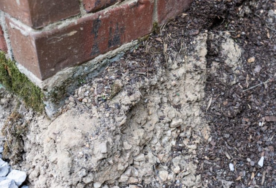Eroded sandy soil and crumbling foundation, showing how soil conditions make foundations vulnerable to sinking in Jacksonville, FL.