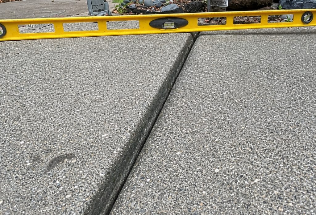 Level tool in a cracked concrete driveway surface showing vertical displacement needing driveway crack repair in Ocala, FL.