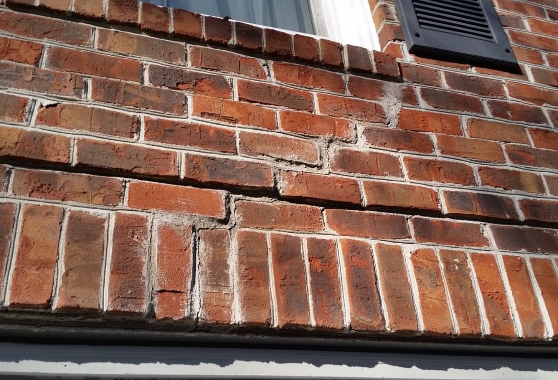 Stair-step zigzag cracking pattern through brick mortar exterior wall showing signs of sinking foundation in St Augustine, FL.