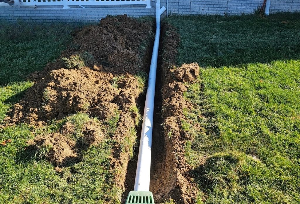Downspout extension in Jacksonville, FL, installed in yard trench with drain outlet redirecting roof runoff away from foundation.