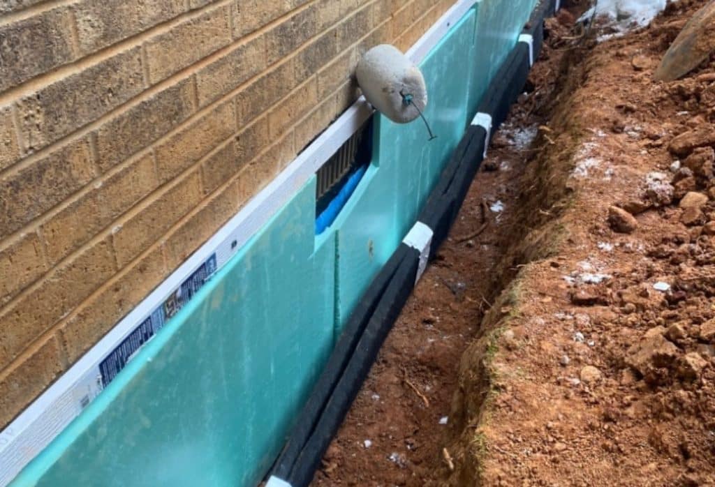Exterior foundation drainage system in Gainesville, FL, showing waterproof membrane and drain board installed along foundation wall.
