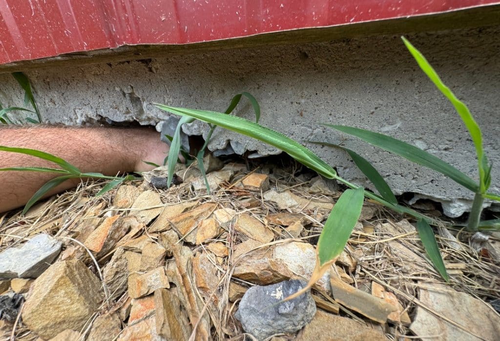 A large void beneath a damaged concrete wall with a hand inserted into the gap during an exterior foundation inspection in Ocala, FL