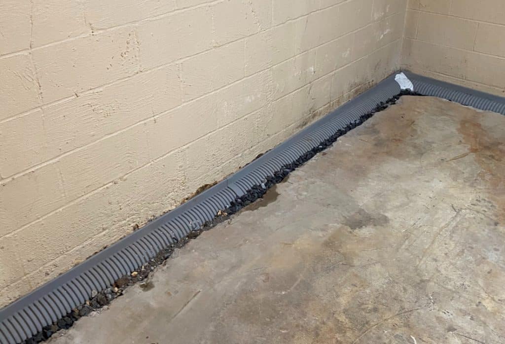 Interior foundation drainage system in St Augustine, FL, with corrugated perforated pipe installed along concrete block wall perimeter.