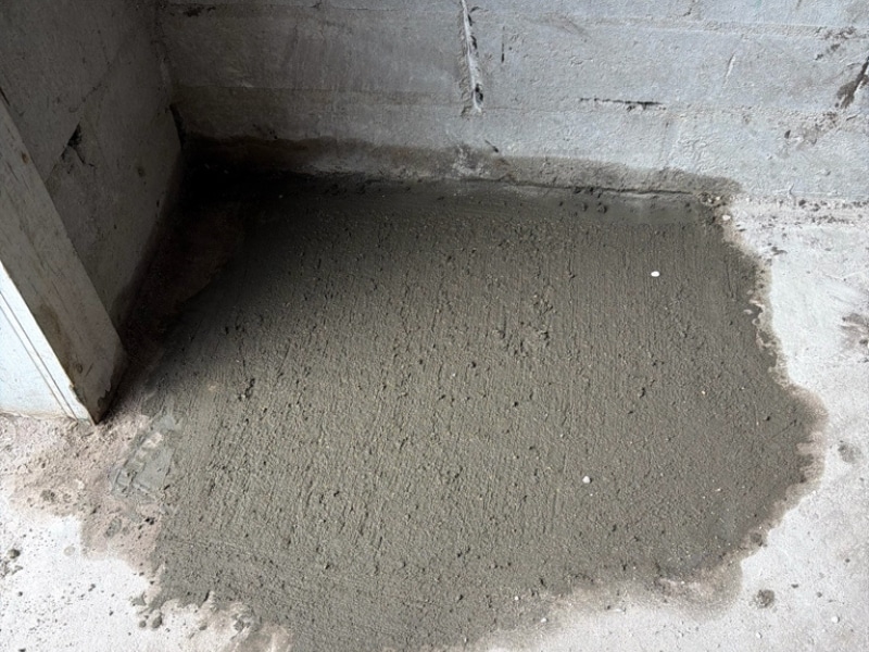Concrete floor patched with fresh concrete in laundry room corner after helical pier installation in Neptune Beach, FL.