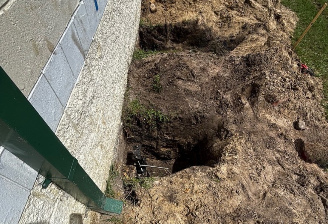 Excavated trench with push pier brackets and hydraulic ram seated at commercial building foundation wall in Jacksonville, FL.