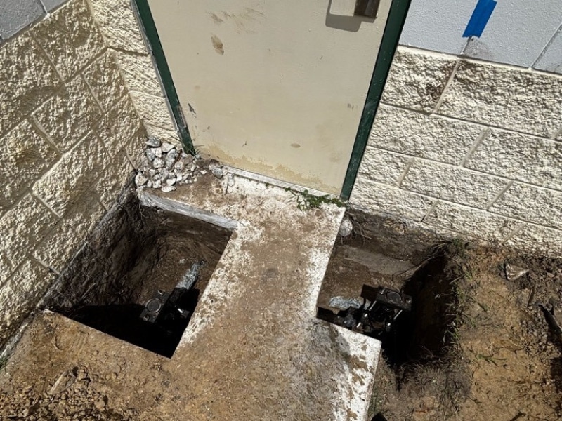 Push pier brackets installed at foundation footing beside service door during commercial foundation repair in Jacksonville, FL.