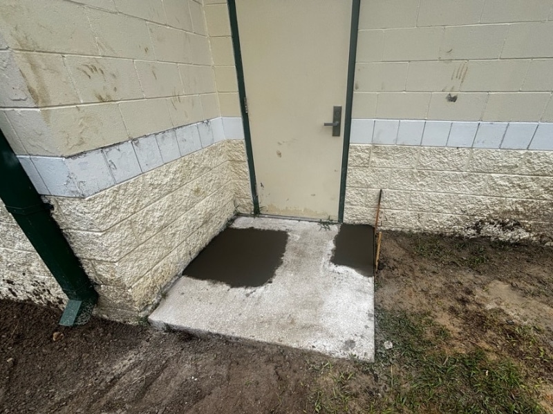 Fresh concrete patches over pier locations beside service door after commercial push pier installation in Jacksonville, FL.