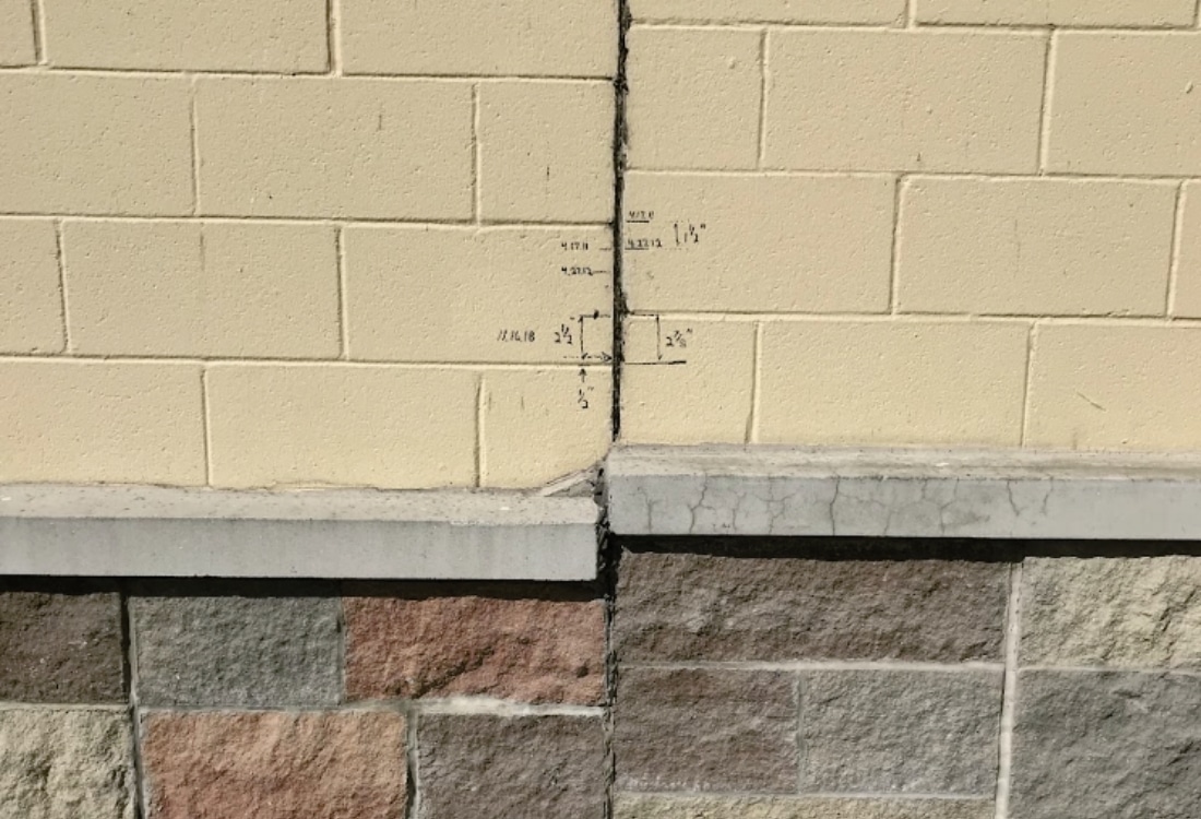 Close-up of a vertical crack on foundation wall with handwritten width measurements to monitor before fixing crack in Jacksonville, FL.
