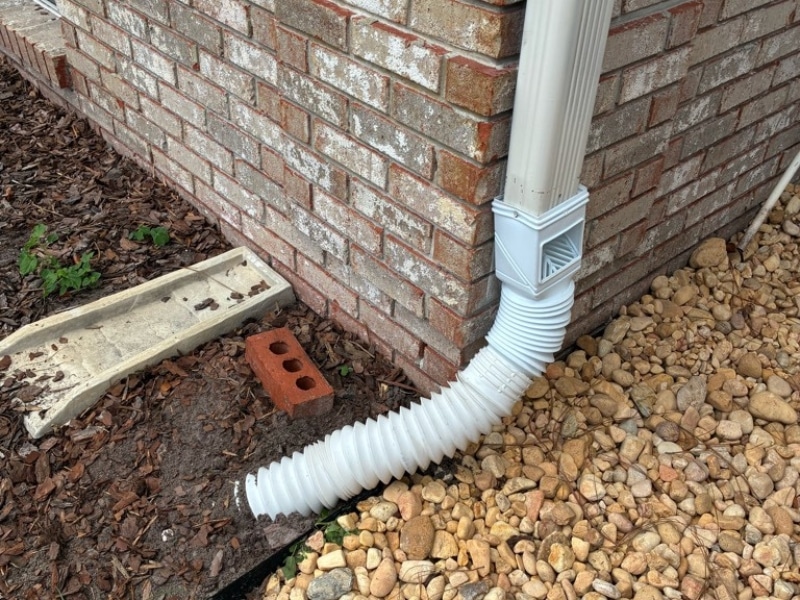 Downspout adapter connected to flexible drain pipe at brick foundation wall in Jacksonville, FL.