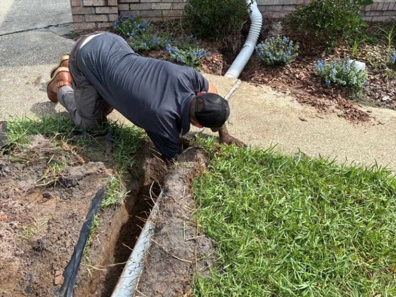 Solid PVC pipe laid in open trench and attached to existing pipe during downspout drainage system installation in Jacksonville, FL.