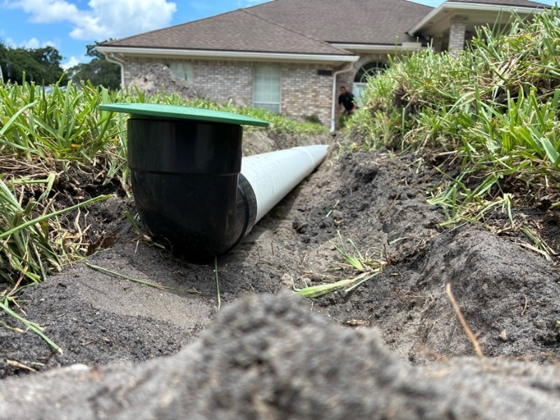 Green pop-up emitter flush in grass at discharge point after downspout drainage installation in Jacksonville, FL.